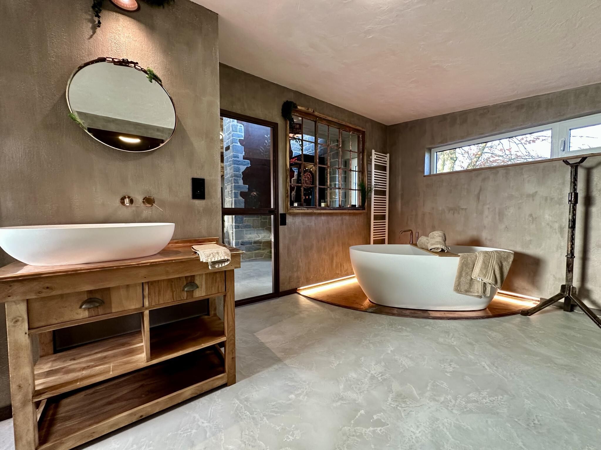 Een moderne badkamer met een vrijstaand bad, een groot ovaal wastafel en een houten wastafelmeubel.