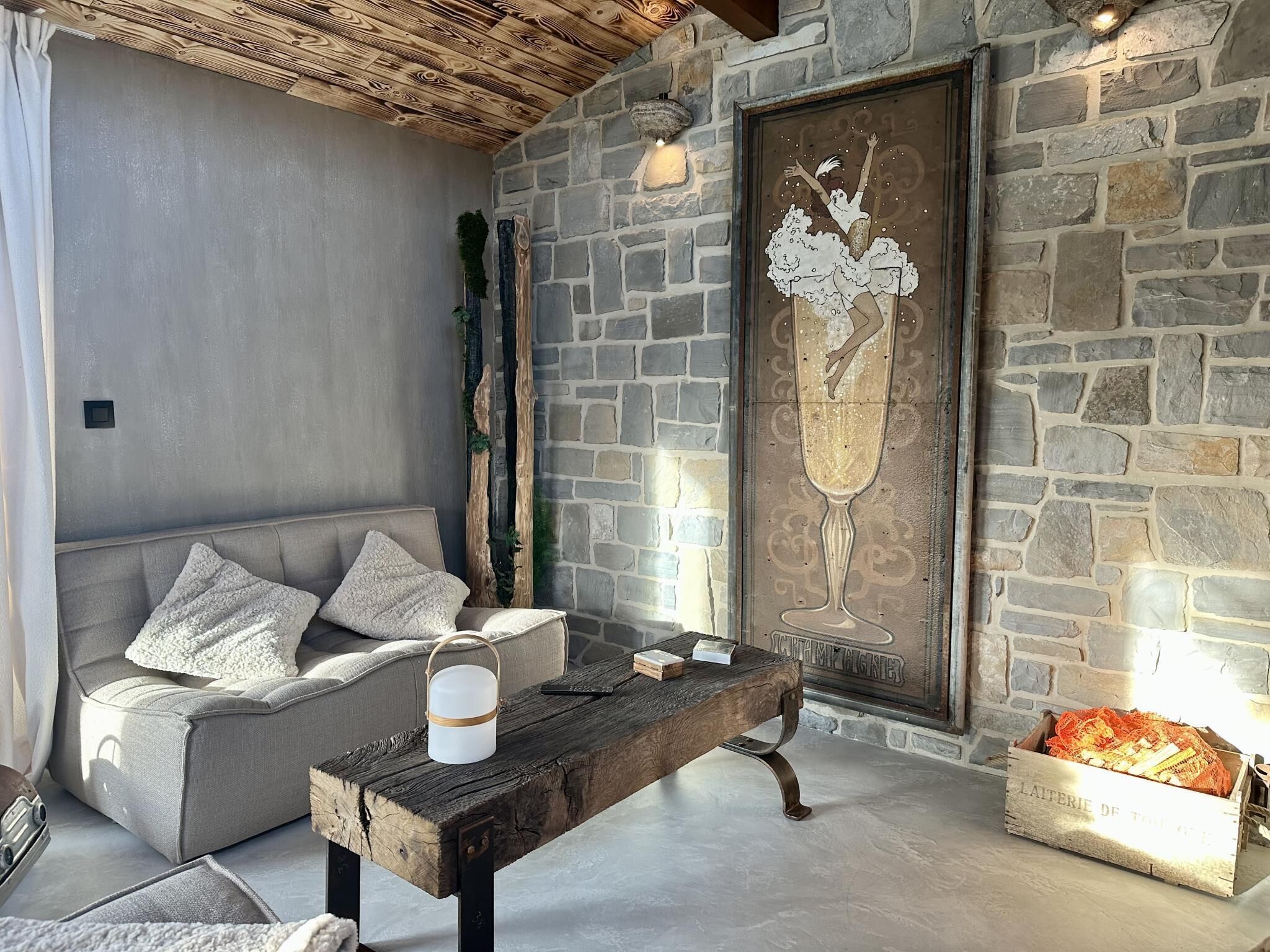 A cozy living room with a stone wall, a wooden bench, a grey sofa, and a decorative glass piece.