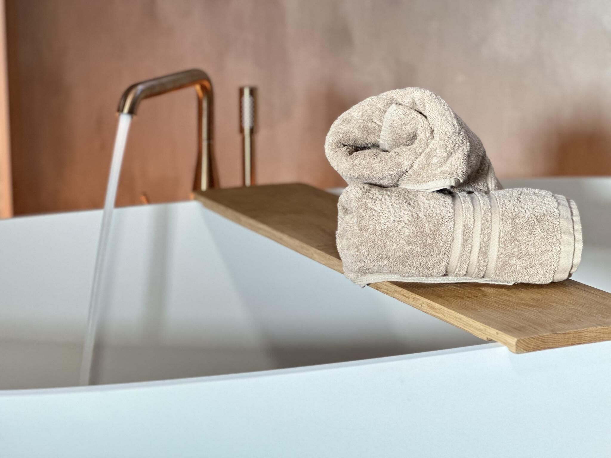 A bathtub with a wooden shelf holding a rolled towel.