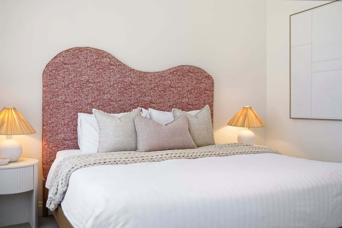 A neatly made bed with a textured headboard, two bedside lamps, and a framed picture on the wall.