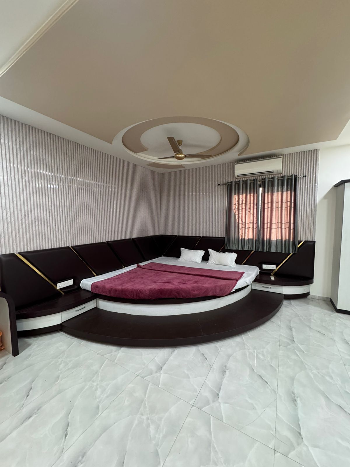 A modern bedroom with a curved bed, a ceiling fan, and a window with curtains.