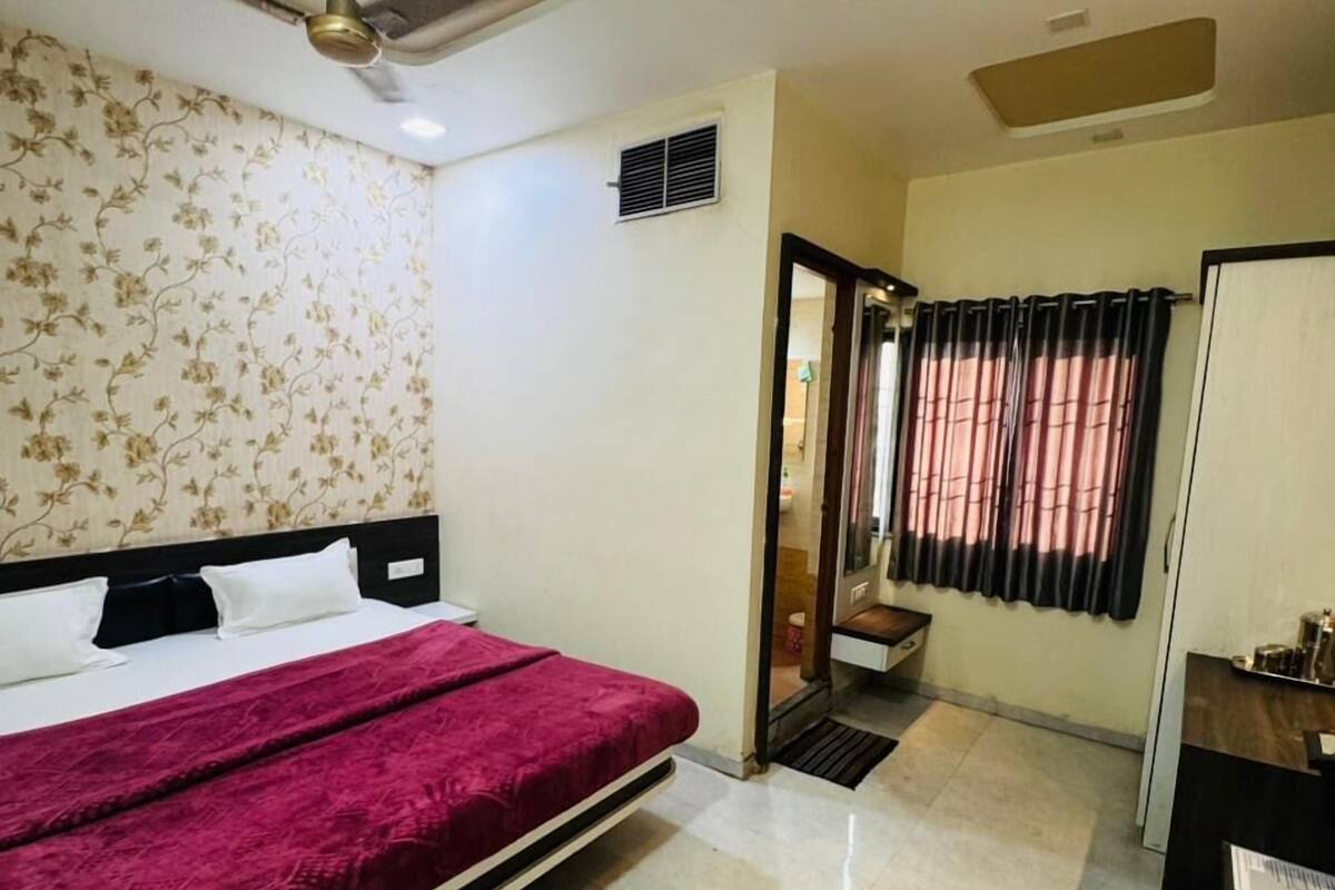 A hotel room with a bed, a ceiling fan, a small window with curtains, and a desk with a mirror.