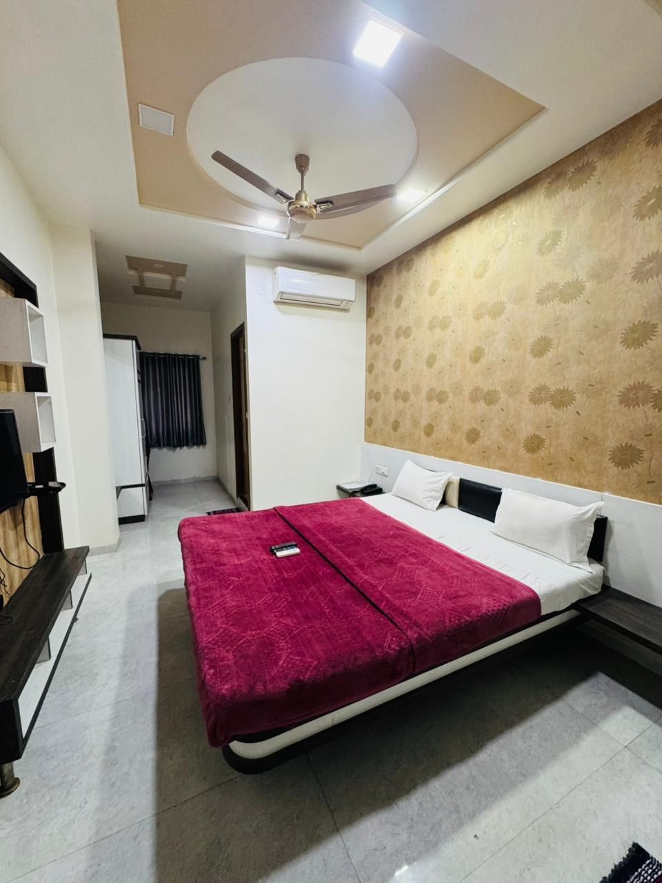 Quarto de hotel com cama, ventilador de teto, ar condicionado, televisão e escrivaninha.