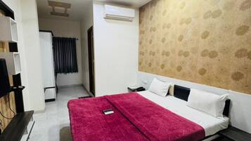 Quarto de hotel com cama, ventilador de teto, ar condicionado, televisão e escrivaninha.