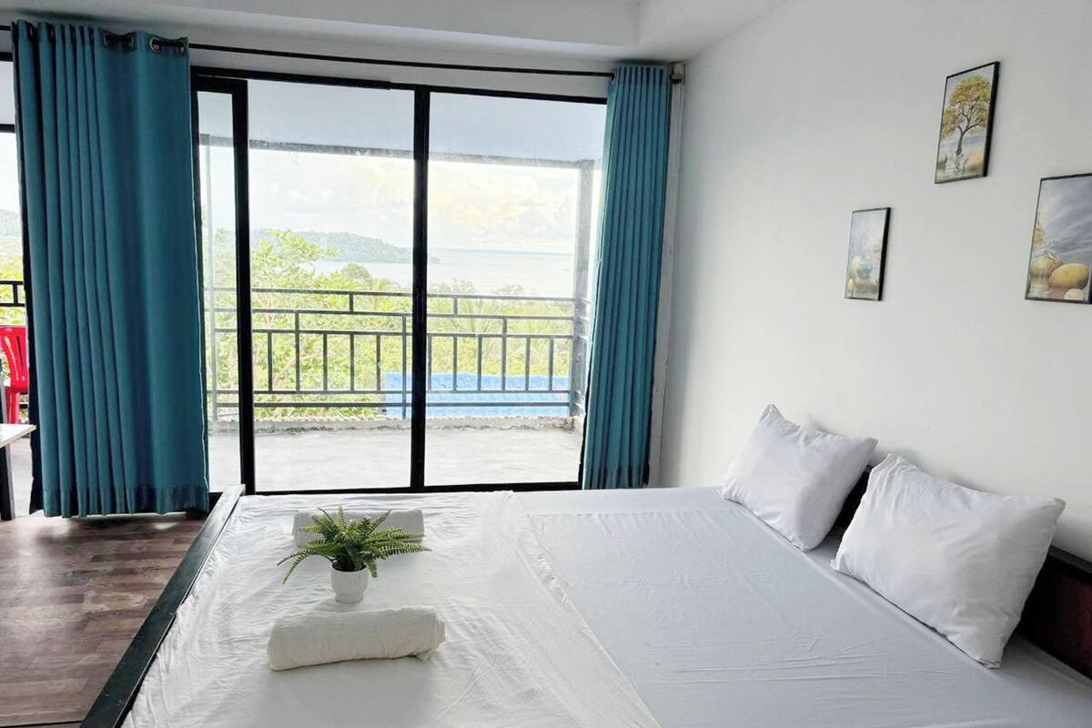 A hotel room with a large bed, a view of the outdoors through a sliding door, and a small plant on the bed.