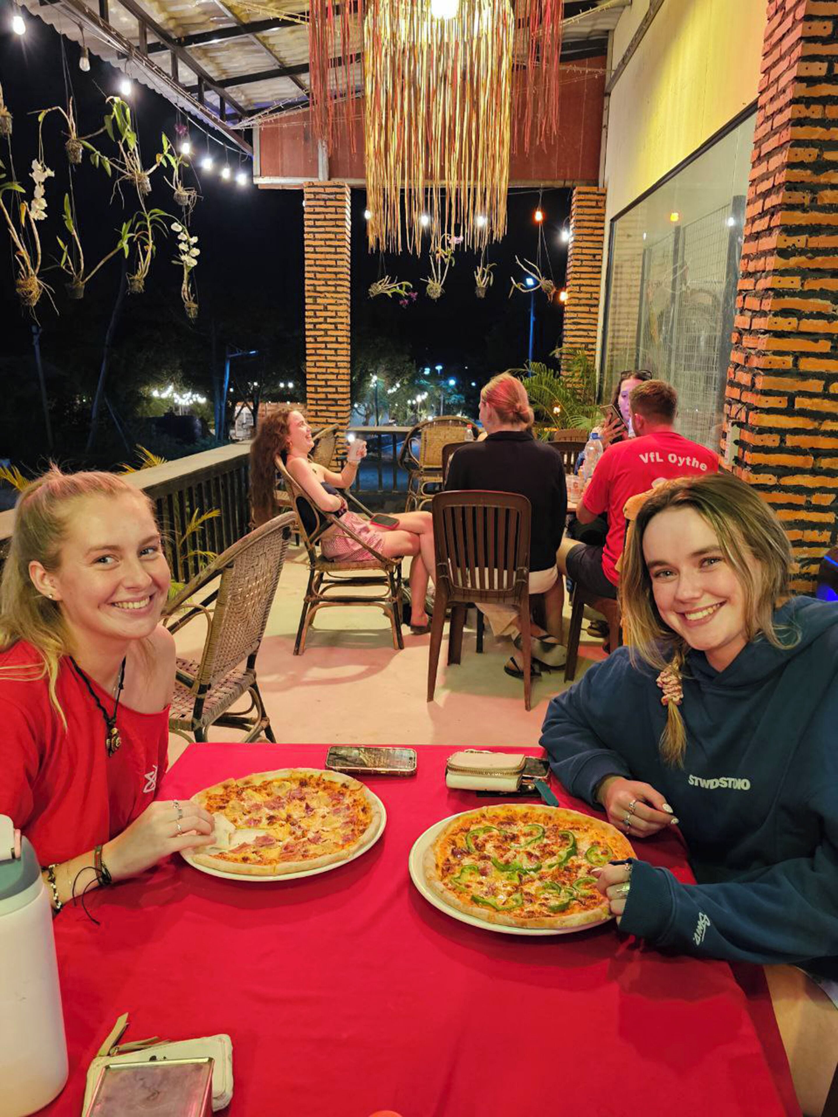 An outdoor dining area with brick pillars, hanging decorations, and tables with pizza.