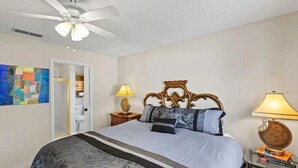 Quarto com cama, ventoinha no teto, mesa de cabeceira com abajur e luminária na parede.