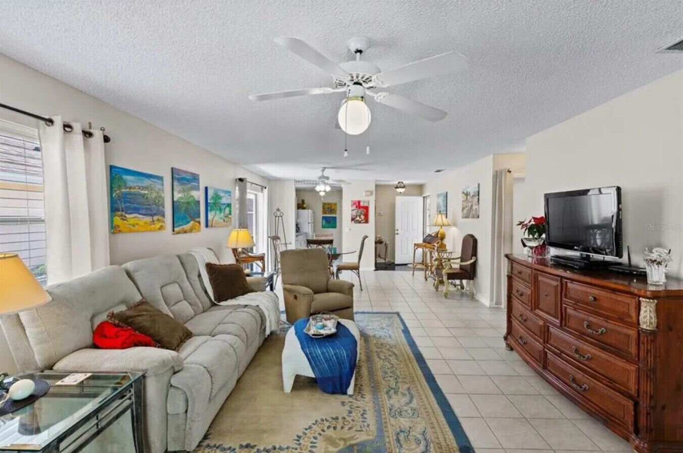 A living room with a sofa, armchair, coffee table, TV, and a ceiling fan.