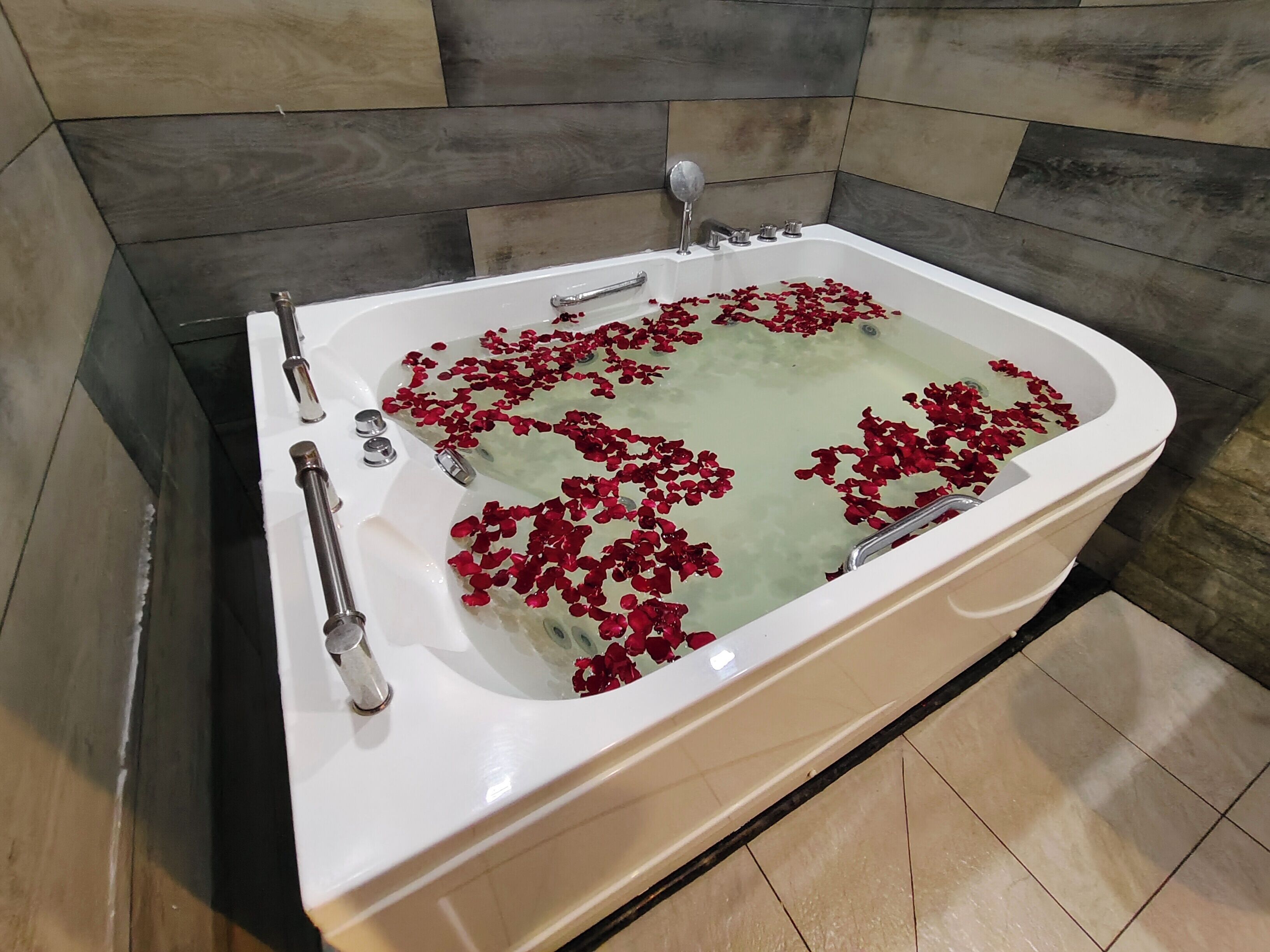 A bathtub with rose petals floating on the water, surrounded by tiled walls.