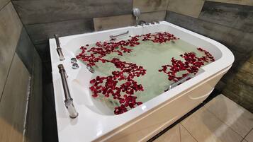 A bathtub with rose petals floating on the water, surrounded by tiled walls.