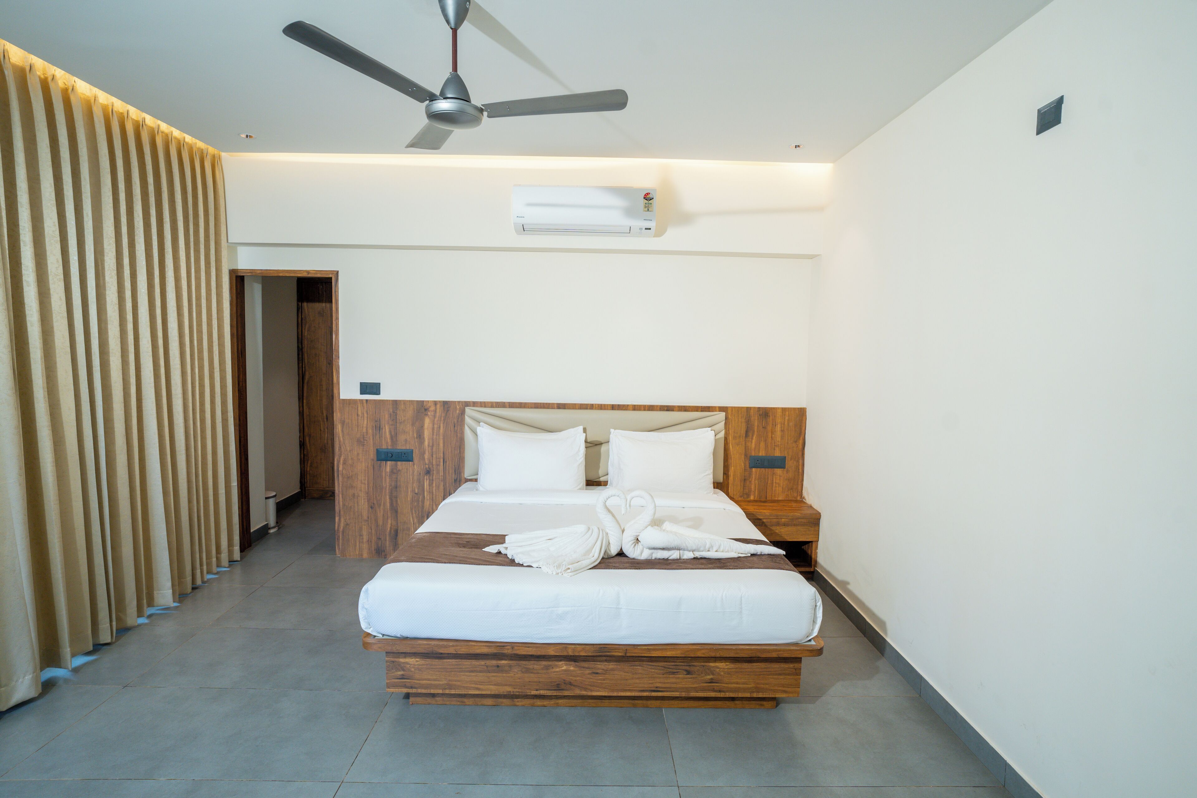 Une chambre d’hôtel équipée d’un lit, d’un ventilateur de plafond, d’un appareil de climatisation et d’une tête de lit en bois.