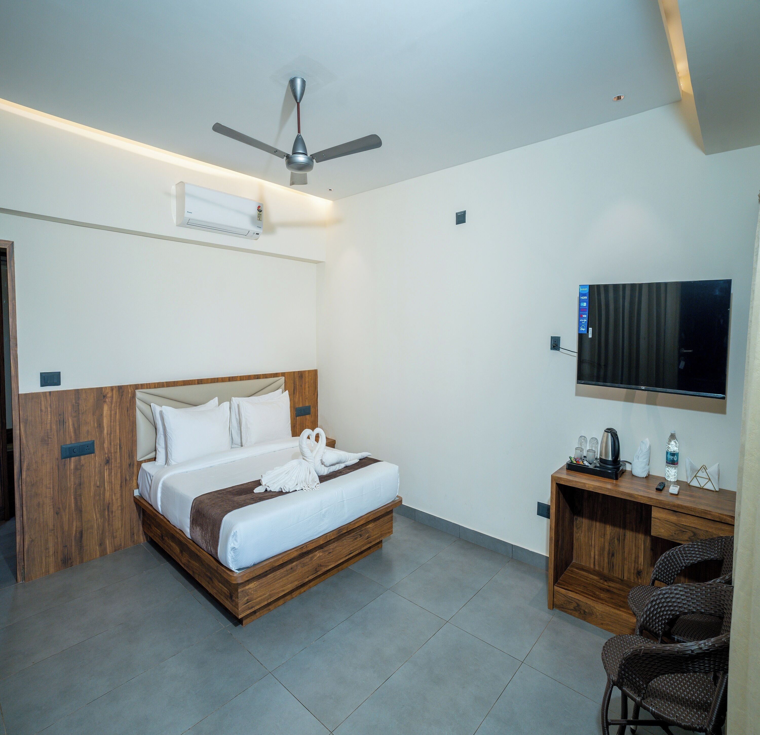 Una habitación de hotel con cama, escritorio, silla, televisor y ventilador de techo.