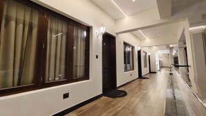 Un couloir d’hôtel moderne, doté d’un plancher en bois, de grandes fenêtres avec des rideaux et d’un long couloir avec des portes des deux côtés.