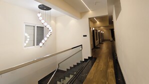 Un couloir d’hôtel moderne avec un escalier, un luminaire décoratif et une rangée de portes.