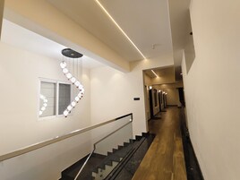 Un pasillo moderno de hotel con una escalera, un aplique decorativo y una fila de puertas.