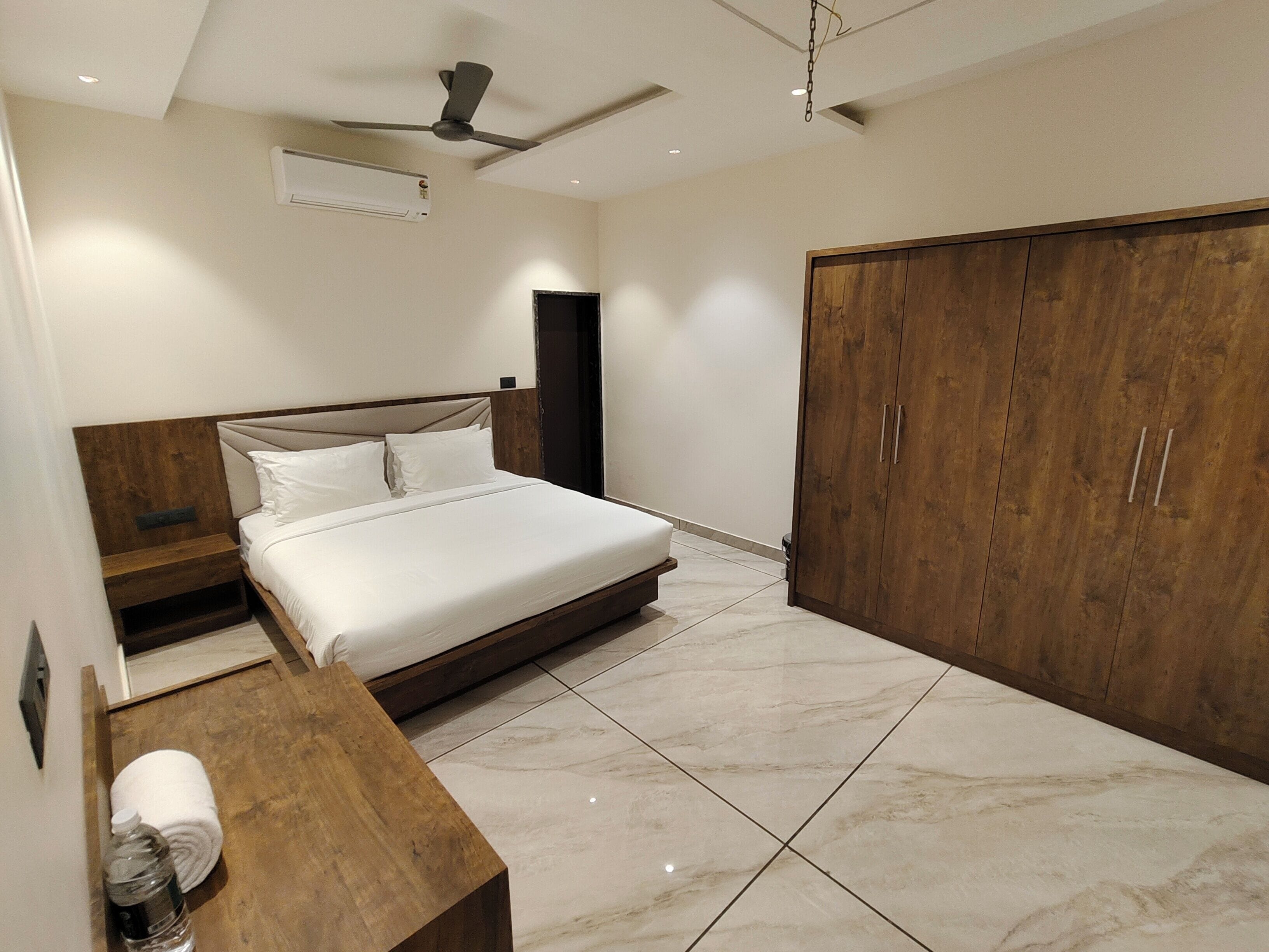 A bedroom with a bed, wooden bedside table, a wardrobe, and a ceiling fan.