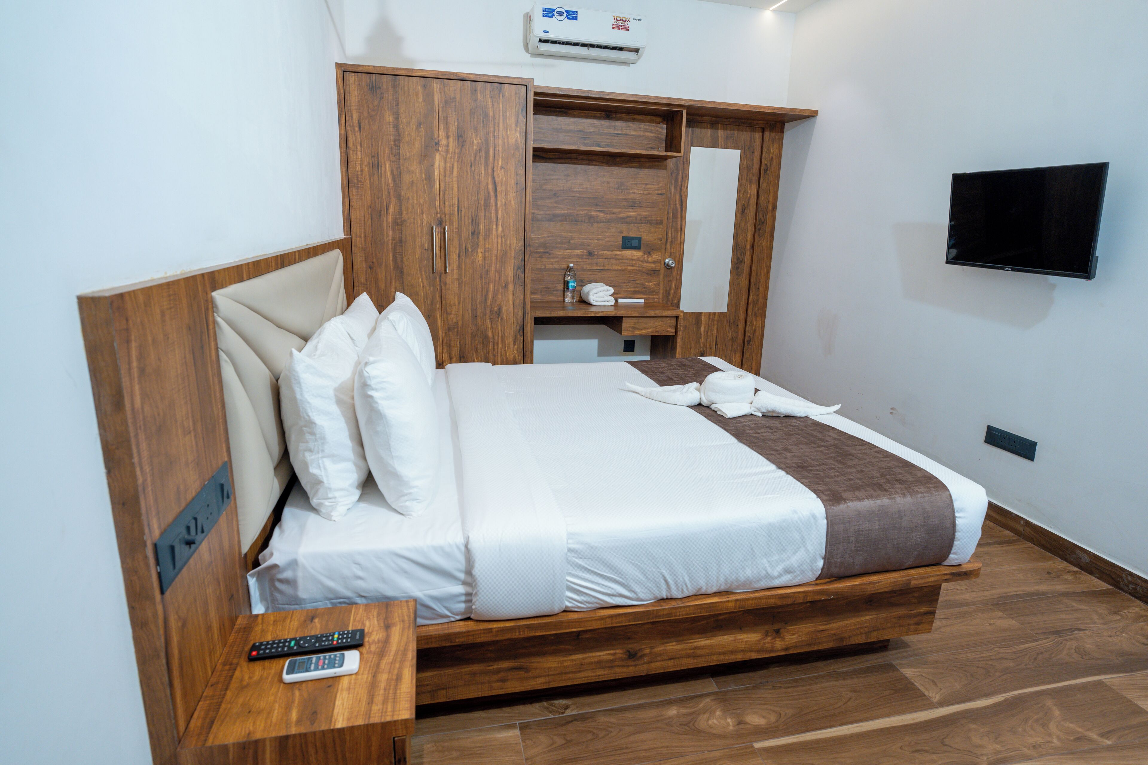 A bedroom with a wooden bed frame, a TV mounted on the wall, and a wardrobe with a mirror.