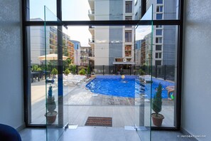 A view of a swimming pool area with lounge chairs and potted plants, surrounded by modern buildings. - Hotel Talgha (Batumi)