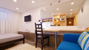 A hotel room with a bed, a desk with a chair, a sofa, a large mirror, a TV, a kitchen area with a microwave, and a view of a bridge. - Compact Romantic Studio for couple (located in semi semi-basement) (Riga)
