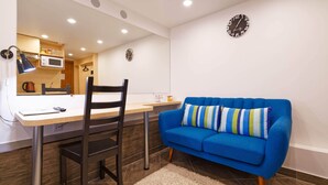 A modern room with a dining table, a blue sofa, a chair, a clock, and a microwave. - Compact Romantic Studio for couple (located in semi semi-basement) (Riga)