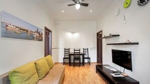 A living room with a sofa, TV, wooden flooring, ceiling fan, and a dining area with chairs and table. - One bedroom Twin apartment in the center of Riga (Riga)