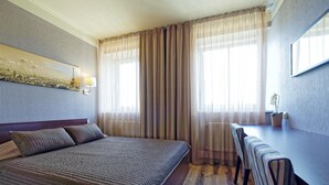 A hotel room with a bed, a desk, and a chair. There is a window with curtains, a wall-mounted lamp, and a small potted plant. - Two bedrooms, Two double beds, 8 persons (Riga)