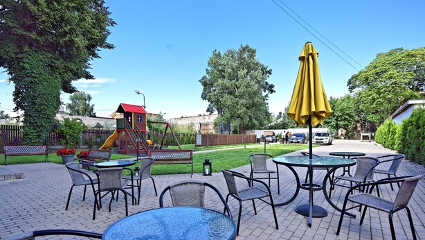 An outdoor patio area with tables and chairs, a playground, and a yellow umbrella. - Double room, small kitchen, 2 persons (Riga)