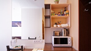 A compact kitchenette with a microwave, kettle, and various food items on shelves. - Double room, small kitchen, 2 persons (Riga)