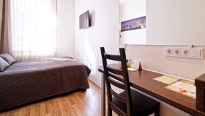 A bedroom with a bed, a wooden desk, a chair, and a television on the wall. - Double room, small kitchen, 2 persons (Riga)