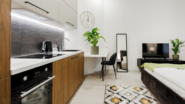 Eine moderne Küche mit Herd, Spüle und Schränken, ein Essbereich mit Tisch und Stühlen, ein großer Spiegel, ein Fernseher und ein Bett mit grüner Decke.
