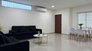 A modern living room with a black sofa, a glass coffee table, and a dining area with white chairs and a table. - Spacious accommodation with excellent location (Mazatlán)