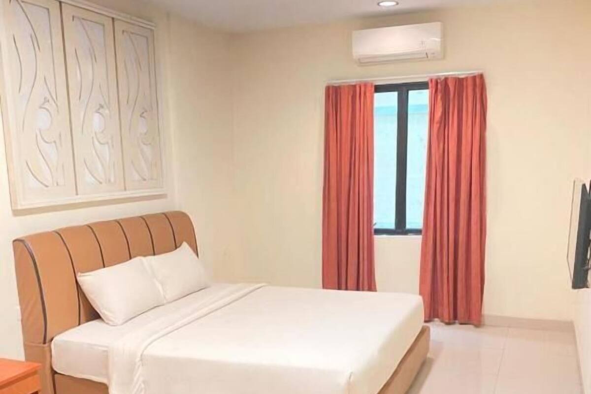 Un dormitorio con una cama, una mesita de noche, un aire acondicionado de pared y una ventana con cortinas.