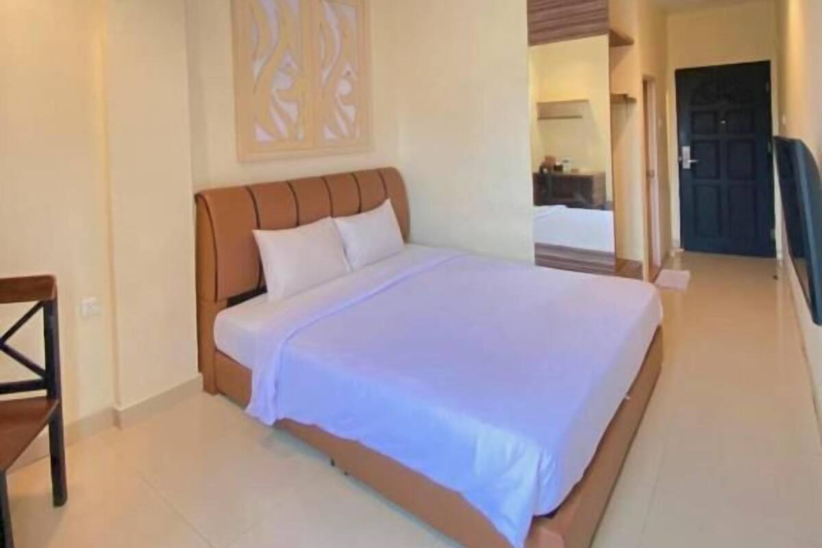 Habitación de hotel con una cama grande, cabecera de madera, panel decorativo en la pared y puerta que da a otra habitación.