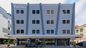 Een modern hotel met een vlakke gevel, veel ramen, en een overdekte parkeerplaats met meerdere motorfietsen.
