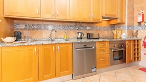A kitchen with wooden cabinets, a stainless steel dishwasher, a microwave, and a gas stove. - Casa da Gina Apartamento T2 com BBQ (Tavira)