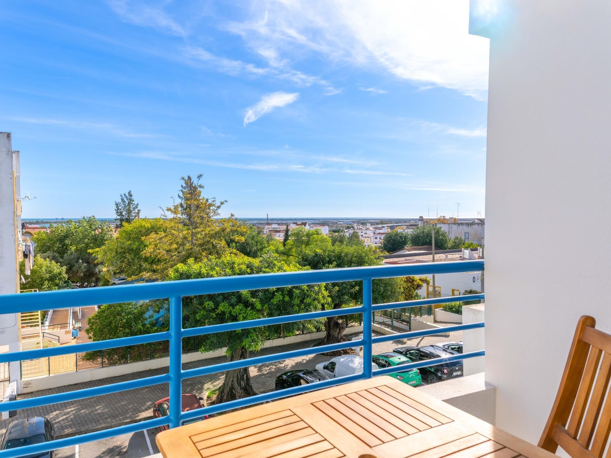 A balcony with a view of a cityscape, trees, and parked cars.