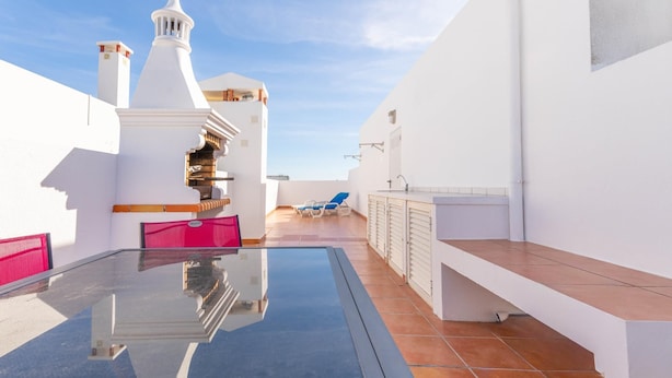 A rooftop terrace with a glass table, a red chair, and a blue chair. - Casa da Gina Apartamento T2 com BBQ (Tavira)