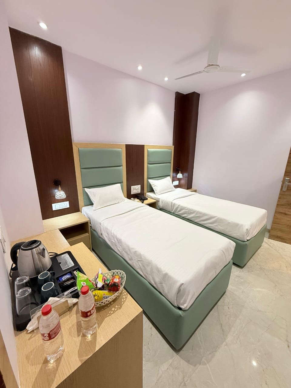 A hotel room with two beds, a desk with a coffee maker, and a basket of snacks.