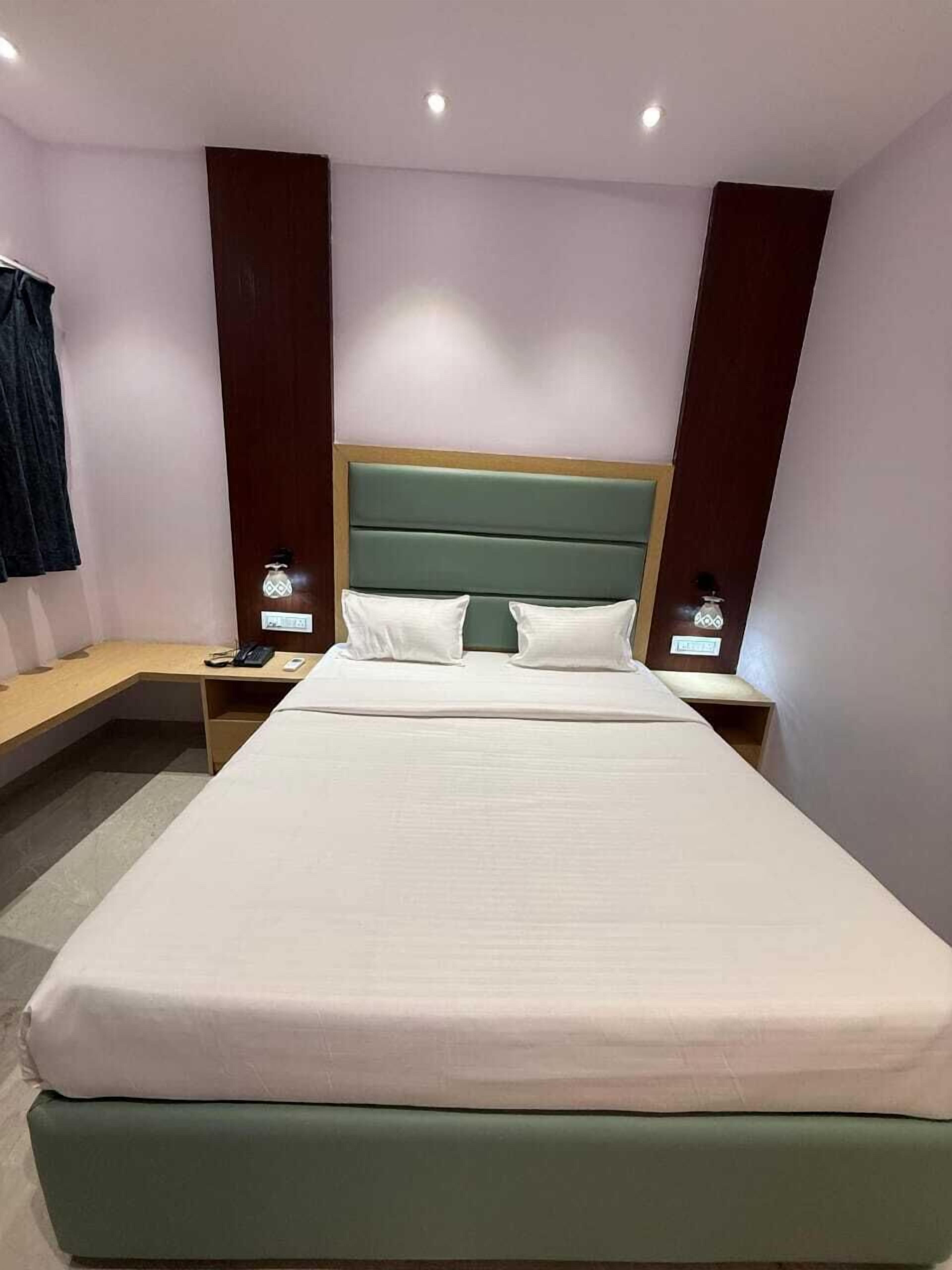 Habitación de hotel con una cama grande, cabecera de madera, dos mesitas de noche con lámparas y un escritorio pequeño con una silla.