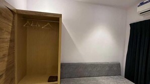 A room with a grey sofa, wooden wardrobe, and a ceiling-mounted air conditioner. - Hotel Grand Soma (Nagpur)