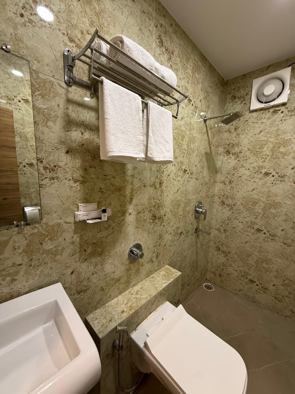 A bathroom with a marble wall, a sink, a toilet, and a shower.