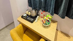 A small room with a yellow chair, a wooden table, a kettle, cups, and snacks. - Hotel Grand Soma (Nagpur)