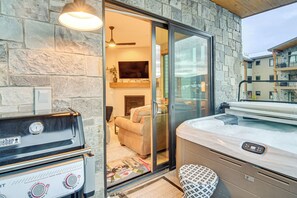 A stone exterior wall, a Weber grill, a sliding glass door leading to a living area with a sofa, and a hot tub. - Walk to Ski Shuttle & Brewery! New Fraser Condo (Fraser)