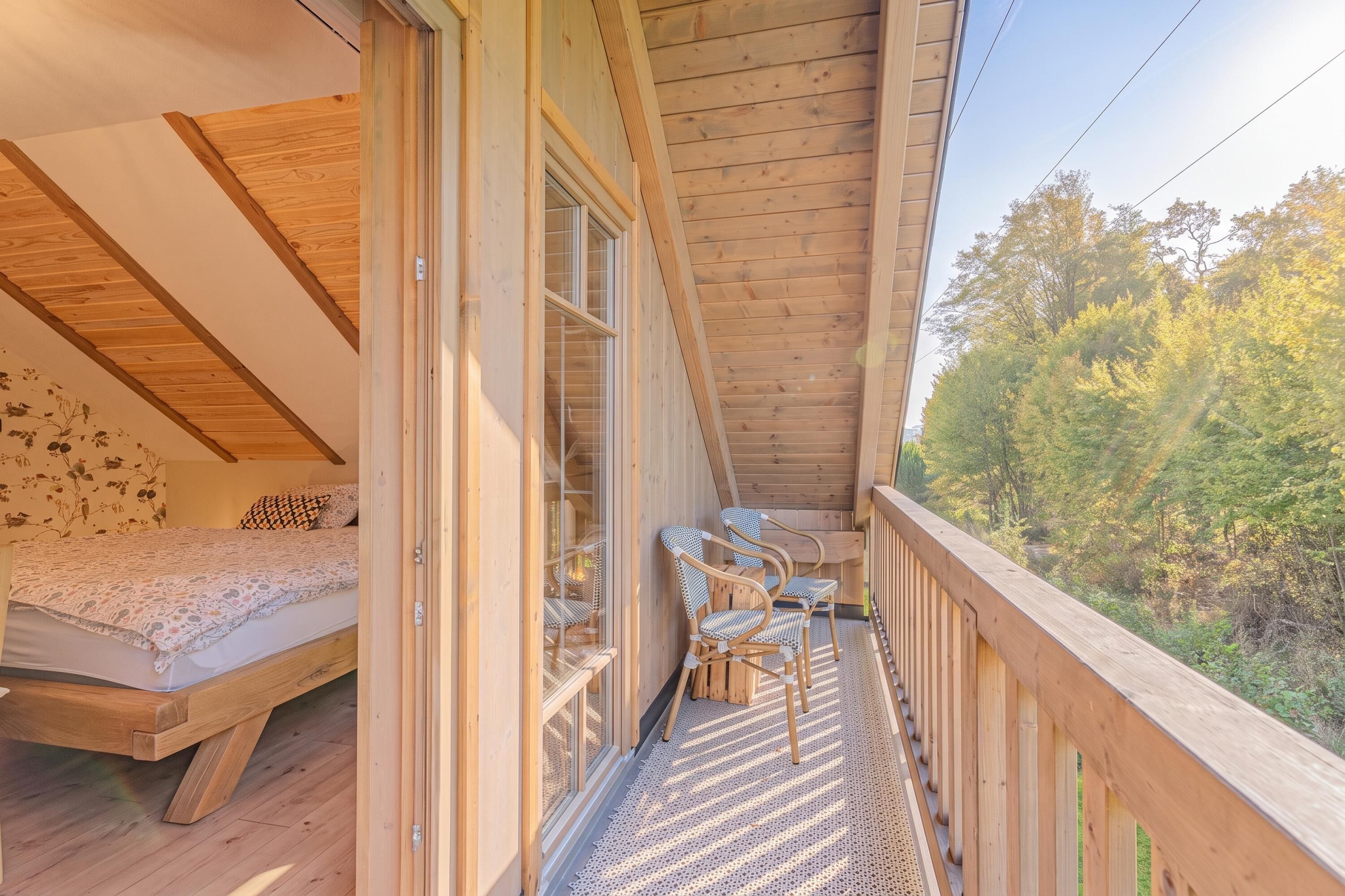 Un balcón de madera con una cama y sillas, con vistas a una zona boscosa.