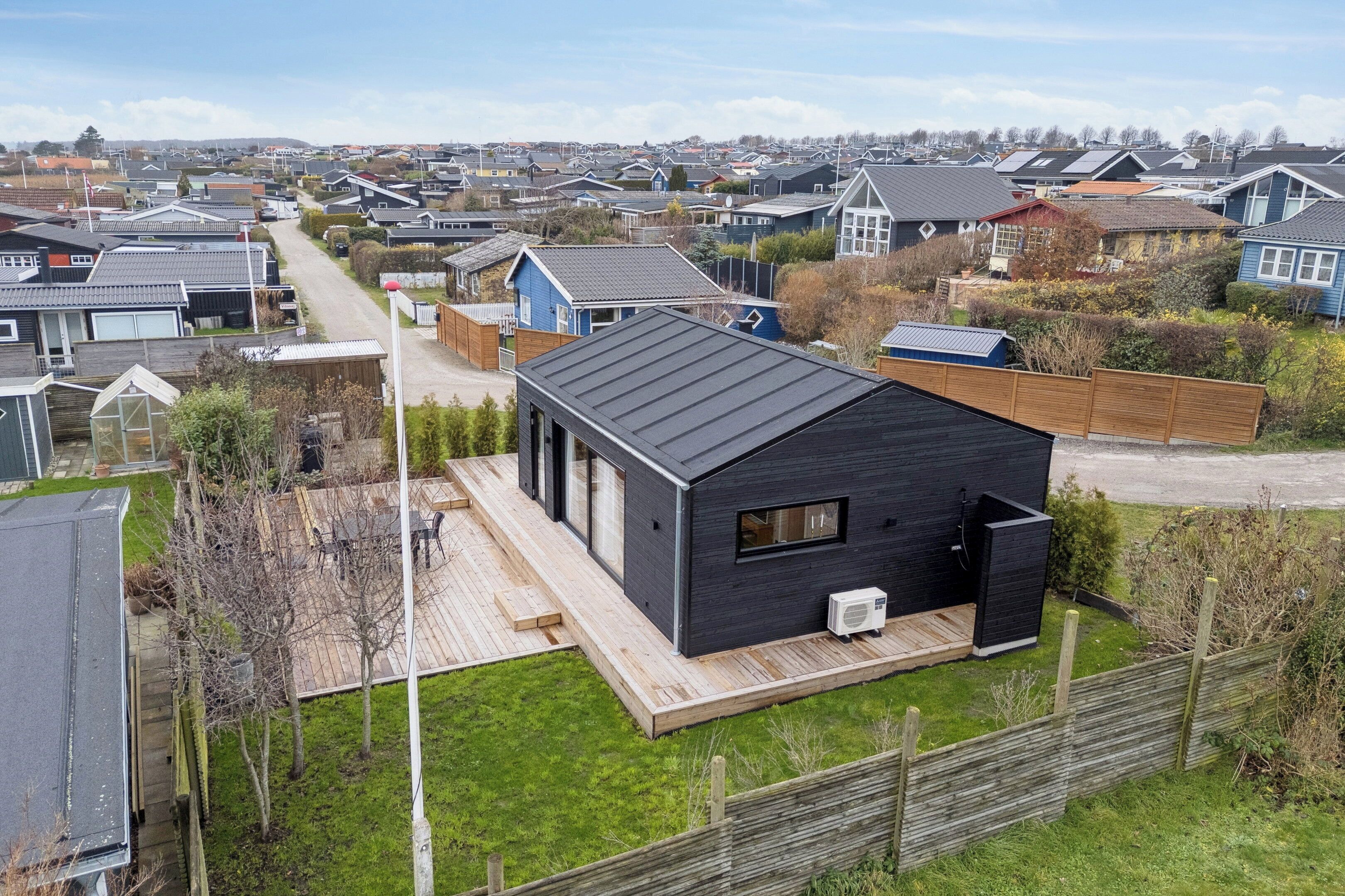A modern house with a large deck, a small attached garage, and a well-maintained lawn.