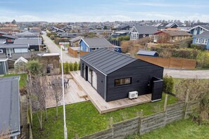 A modern house with a large deck, a small attached garage, and a well-maintained lawn. - Charming newly built cottage 300 m from beach (Karrebæksminde)