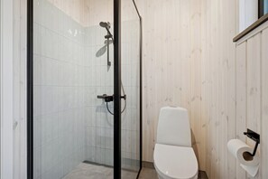 A modern bathroom with a glass-enclosed shower, a white toilet, and a wall-mounted toilet paper holder. - Charming newly built cottage 300 m from beach (Karrebæksminde)