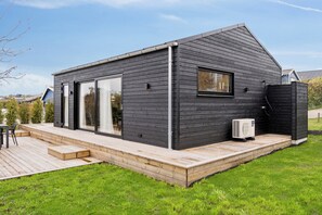 A modern house with a deck, large sliding glass doors, and a small window. - Charming newly built cottage 300 m from beach (Karrebæksminde)