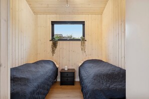 A bedroom with two beds, a window with a view, and a small bedside table with drawers. - Charming newly built cottage 300 m from beach (Karrebæksminde)