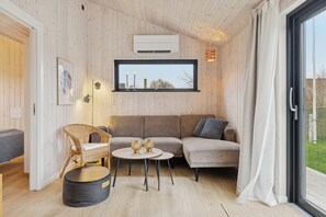 A cozy room with a sofa, a wicker chair, a small table, and a window with a view. - Charming newly built cottage 300 m from beach (Karrebæksminde)